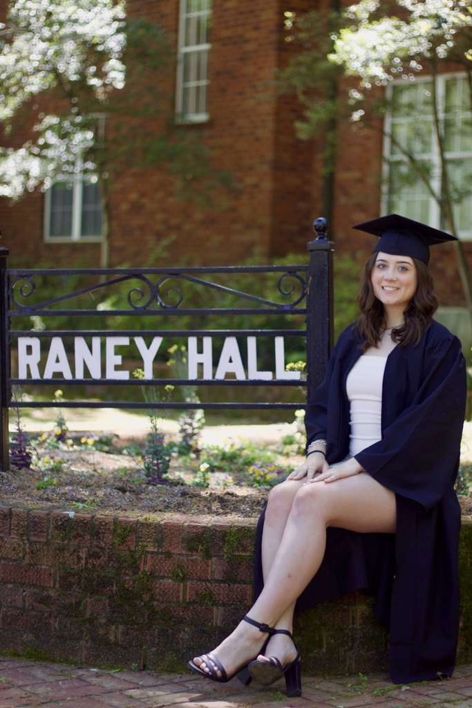 Rye Hazlett sitting in front of Raney Hall in Graduation cap. 
